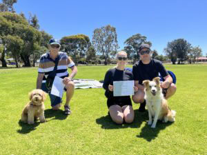 Group of people with dogs during agility training session outdoors.
