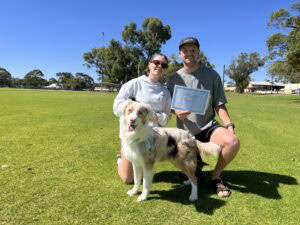 Happy dog trainer with certificate and dog outdoors in park.