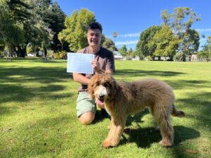 Happy man with certificate and his dog in park, celebrating training success.