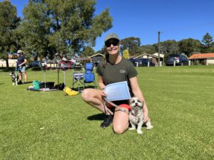 Woman with dog during agility training in park, sunny day.