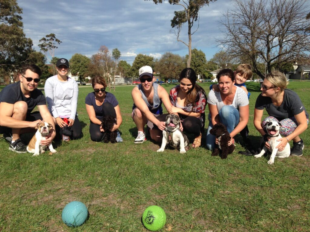 A dog training group with people and puppies outdoors in a park.