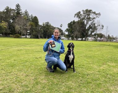 Woman with award and dog at Agile Dogs training session in a park.