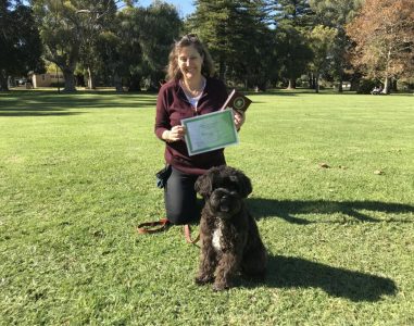 Woman with her dog holding a certificate in a park during daytime.