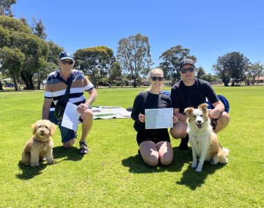 Group of people with dogs during agility training session outdoors.